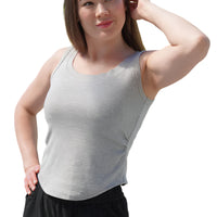Woman wearing a gray tank top and black pants standing outdoors with greenery in the background
