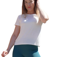 Woman wearing a white t-shirt and teal shorts standing outdoors with trees and a clear sky in the background.