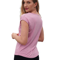 Woman wearing a pink t-shirt and black shorts standing against a dark wall with light accents.