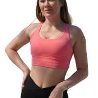 Woman wearing a pink sports bra and black leggings outdoors with greenery in the background