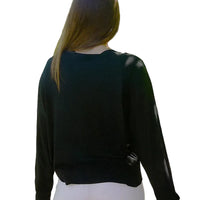 Person wearing a black long-sleeve top and white pants standing in a garden.