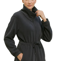 Woman wearing a black jacket with a cowl neck and belt in an outdoor setting.