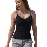 Woman wearing a black tank top and gray pants walking outdoors with trees and buildings in the background.