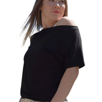 Woman wearing a black off-shoulder top and light-colored pants outdoors with trees and blue sky in the background.