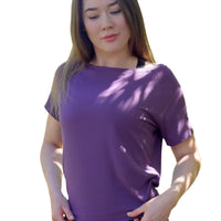 Woman wearing a purple shirt standing outdoors with greenery in the background