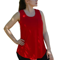 Woman wearing a red tank top and black shorts standing outdoors with greenery in the background