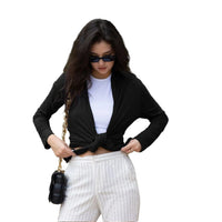 Woman in black cardigan and white pants holding a black handbag outdoors.