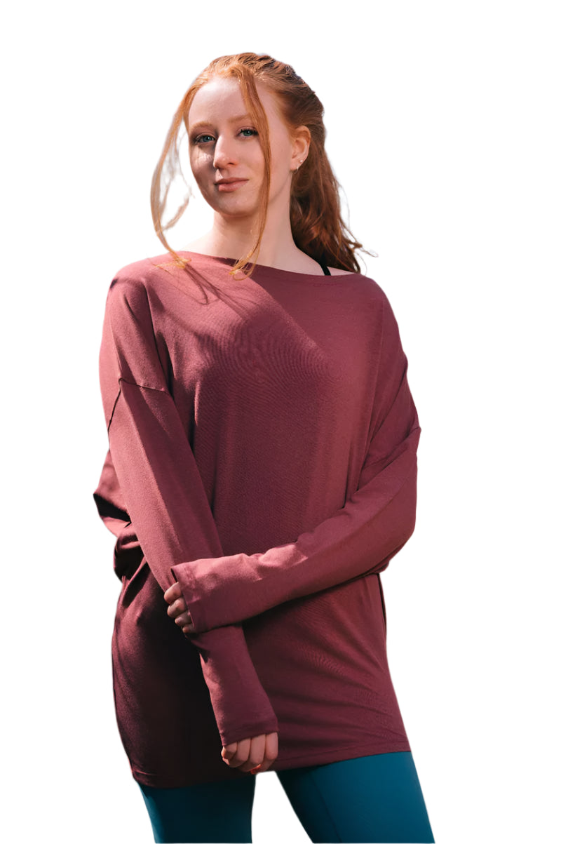 Woman wearing a maroon sweater and blue pants standing outdoors with trees in the background