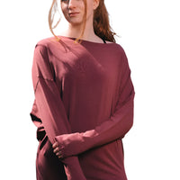 Woman wearing a maroon sweater and blue pants standing outdoors with trees in the background
