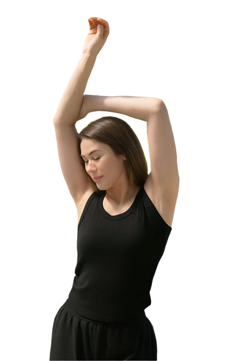 Woman in a black outfit stretching outdoors with green trees and flowers in the background