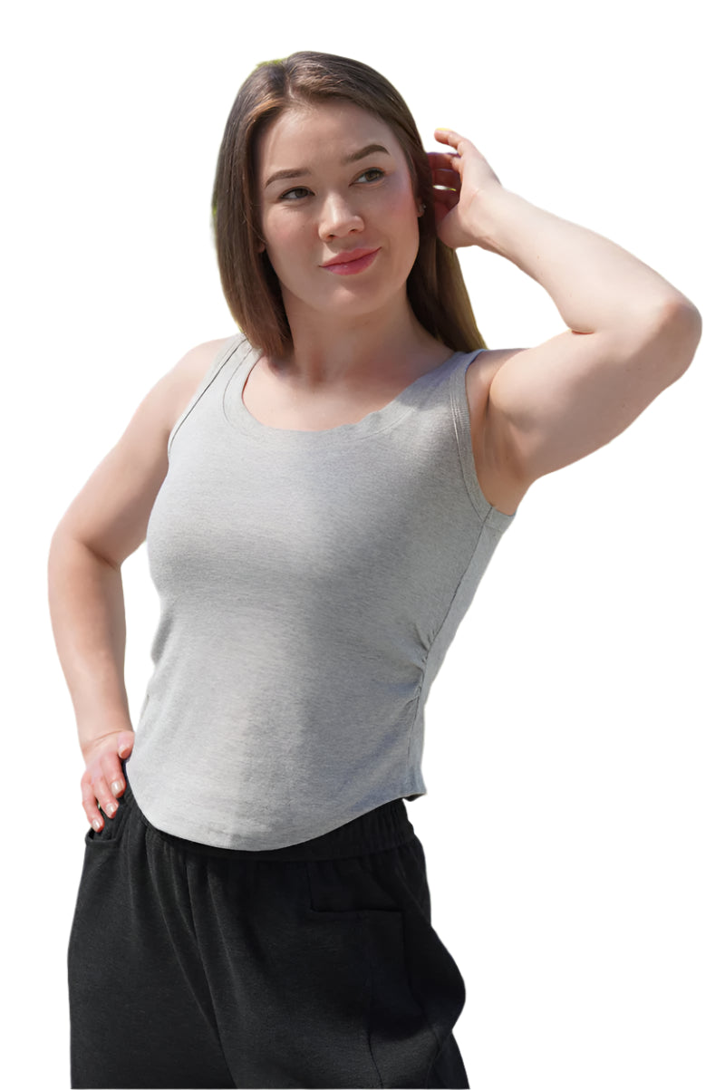 Woman wearing a gray tank top and black pants standing outdoors with greenery in the background