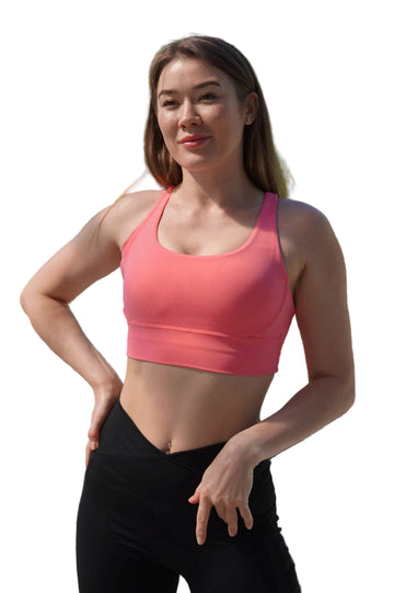 Woman wearing a pink sports bra and black leggings outdoors with greenery in the background