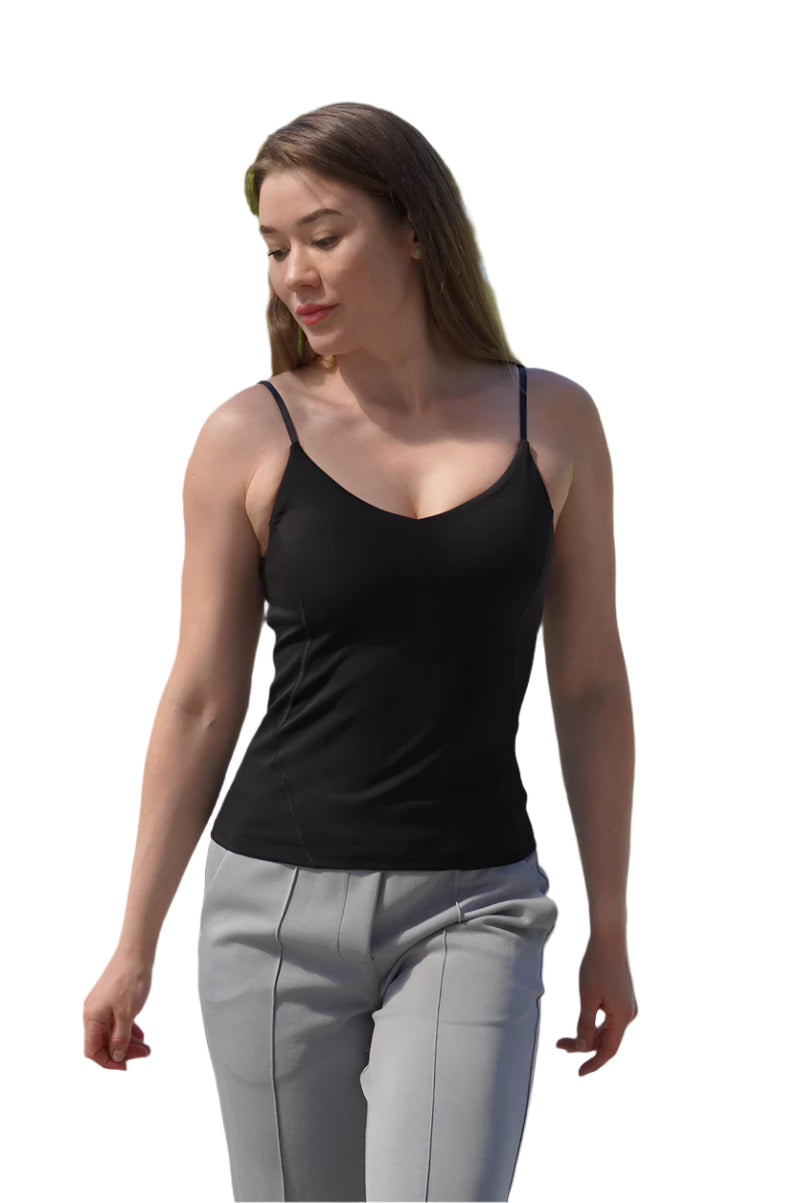 Woman wearing a black tank top and gray pants walking outdoors with trees and buildings in the background.