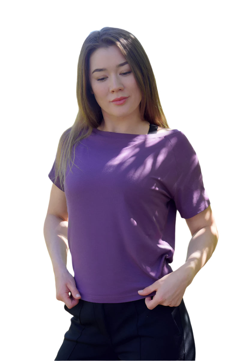 Woman wearing a purple shirt standing outdoors with greenery in the background