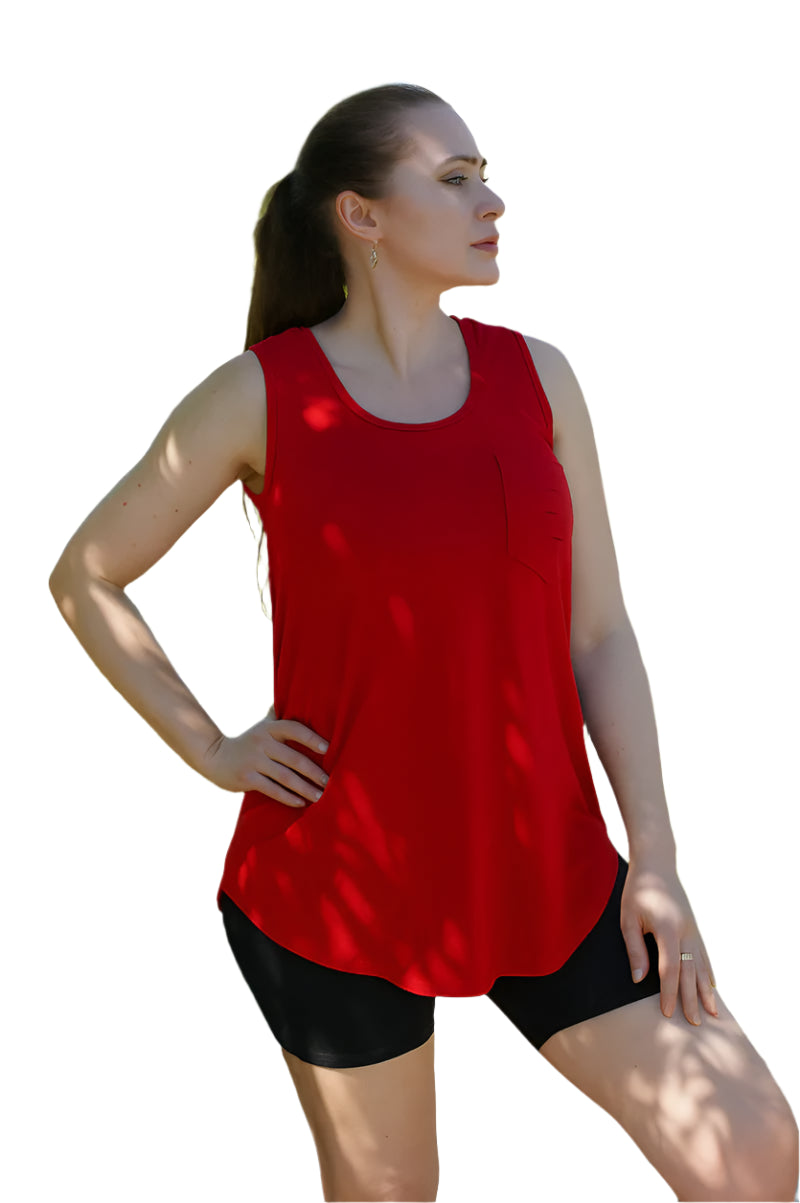 Woman wearing a red tank top and black shorts standing outdoors with greenery in the background