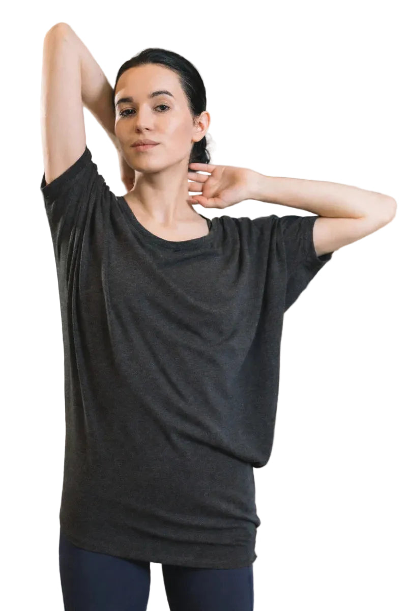 Woman stretching in a yoga studio wearing a black t-shirt and blue pants.