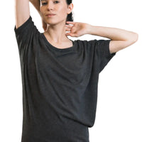 Woman stretching in a yoga studio wearing a black t-shirt and blue pants.